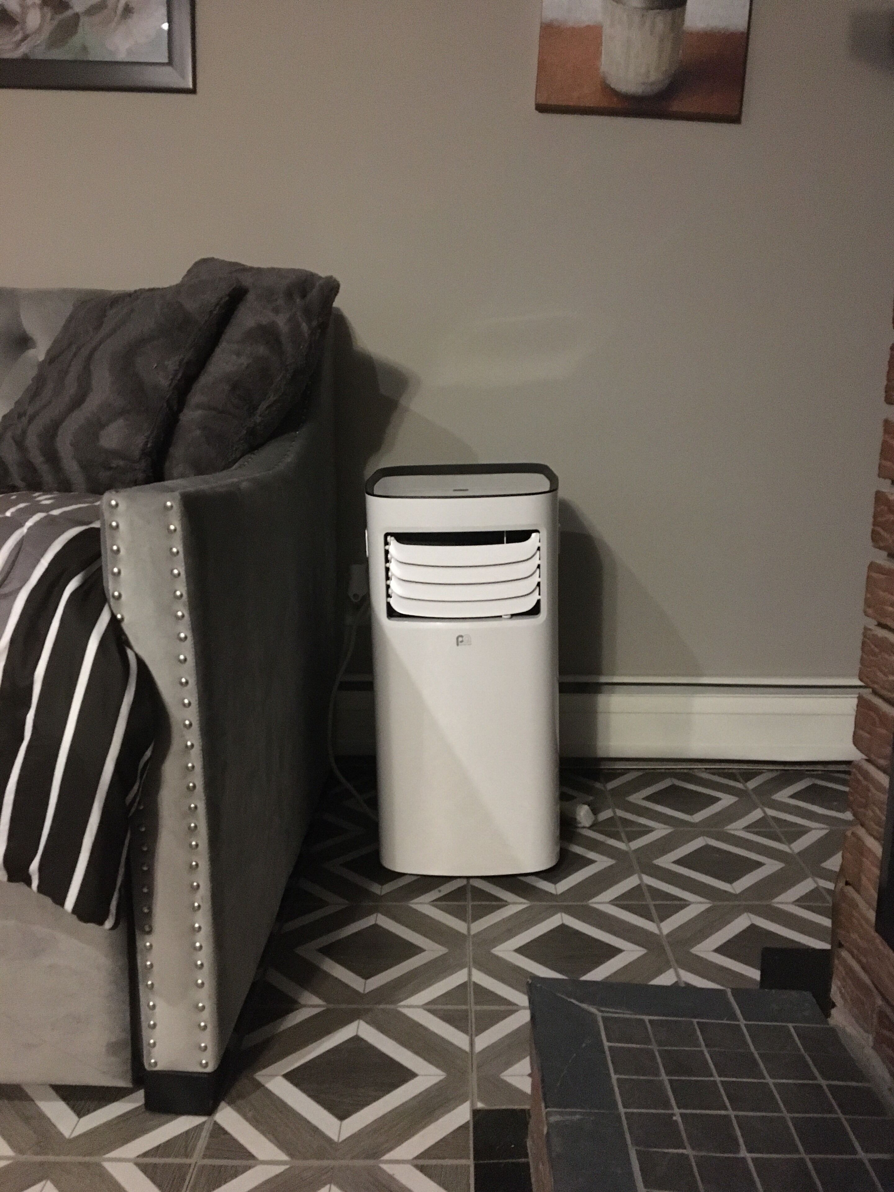 A room with a patterned floor, a grey upholstered sofa with a striped pillow, and a white heater against the wall.