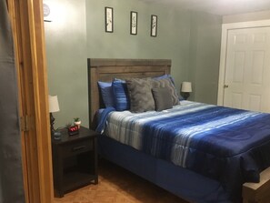 A bedroom with a bed, a nightstand, a lamp, a clock, and a door.