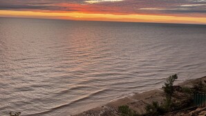 A coastal sunset view with a beach and rocky terrain. - Cottage on the Bluff - NEW Stairs to the Beach, Hot Tub & Unbeatable Sunsets! (South Haven)