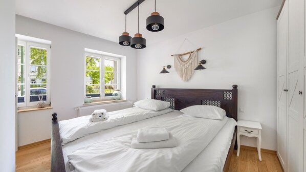 A bedroom with a large bed, two bedside tables, a window with a view of the outside, and a macrame wall hanging.