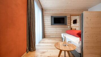 Een kamer met houten lambrisering, een bed, een aan de muur bevestigde televisie en een klein houten tafeltje met een glas erop.