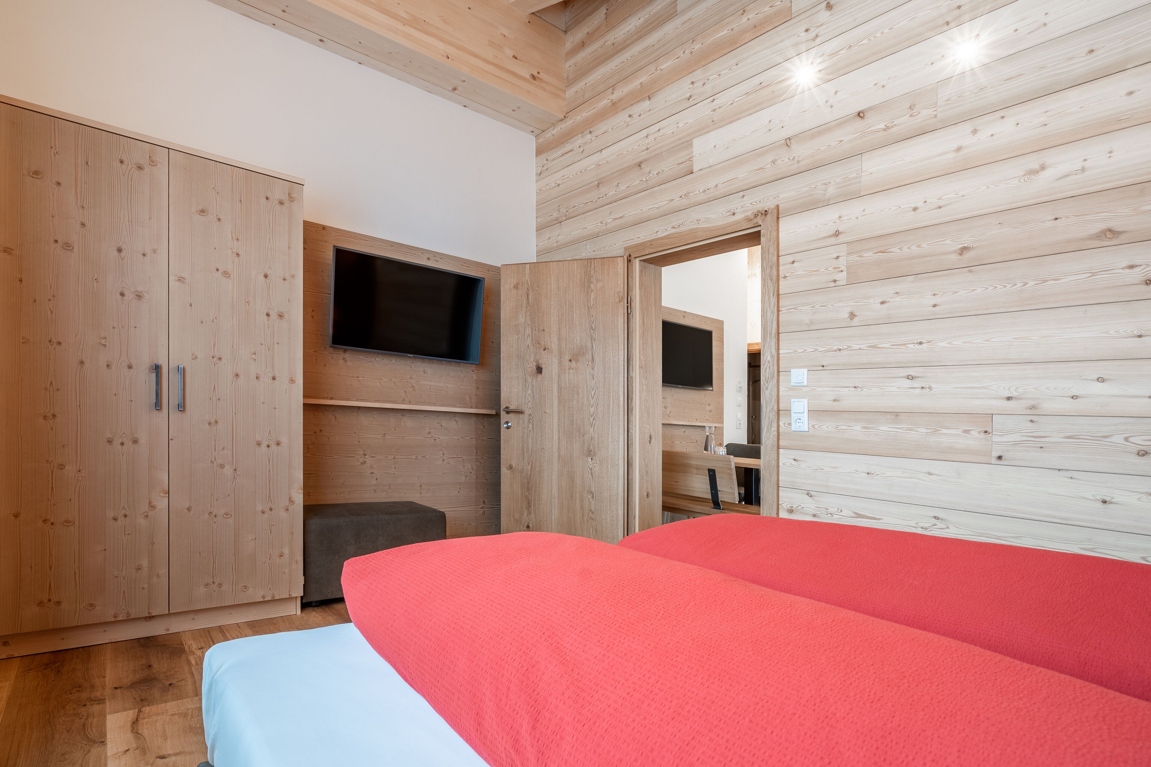 A bedroom with a bed, wooden wardrobe, and a mounted TV.