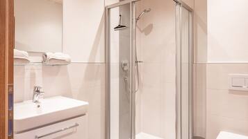 Un baño moderno con techo de madera, ducha con cerramiento de vidrio, lavamanos blanco y un inodoro.