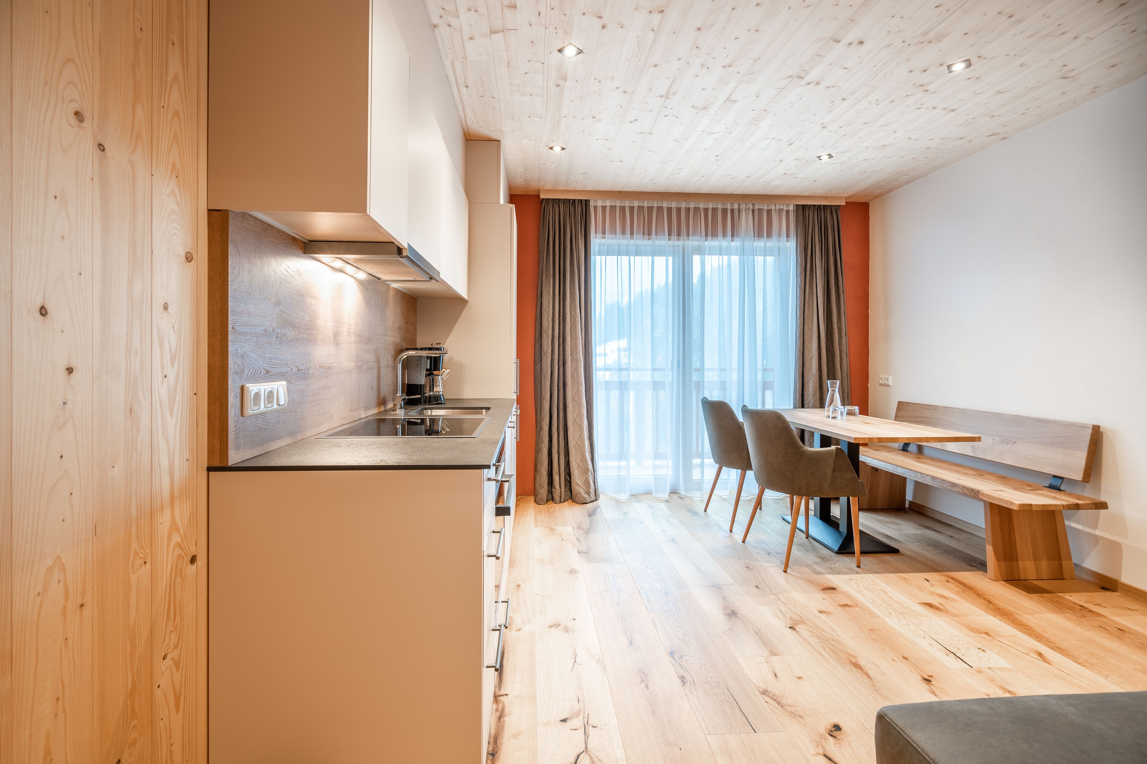 A modern kitchen with wooden cabinets, a built-in stove, and a dining area with a bench and chairs.