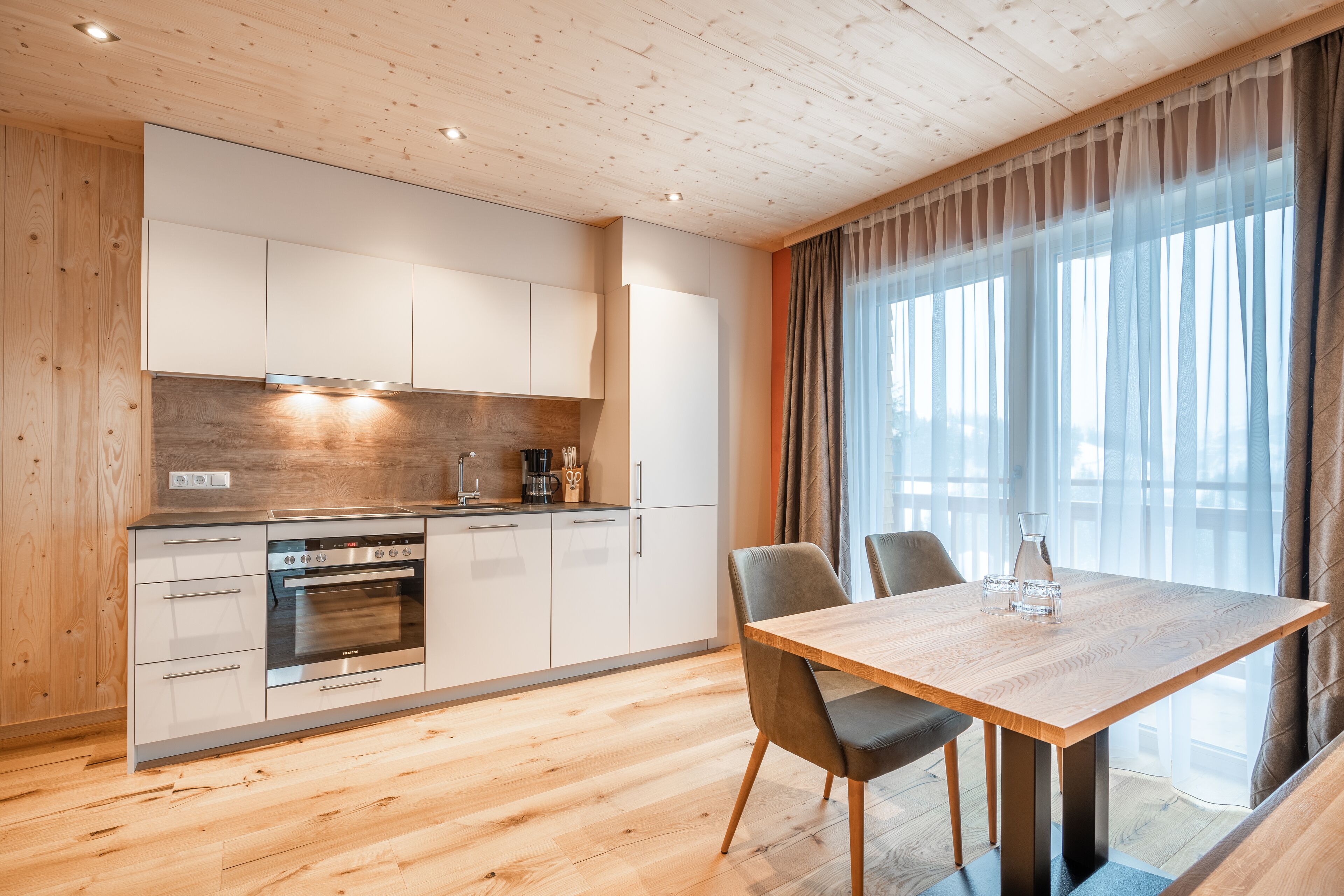 A modern kitchen with wooden cabinets, a built-in oven, and a dining area with a wooden table and chairs.