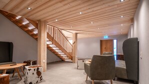 A modern interior with a wooden staircase, a sofa, a table, and a chair. - Naturhaus Gehren (Steeg)