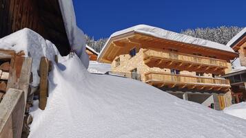 A wooden chalet with a snow-covered roof and balconies, surrounded by a snowy landscape.