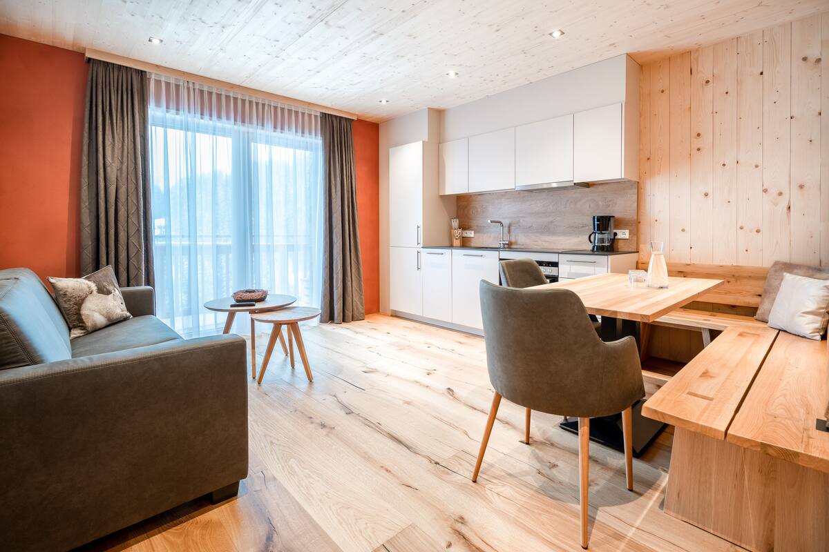 Una sala moderna con un sofá, una mesa de comedor y sillas. Hay una zona de cocina con armarios y una cafetera.