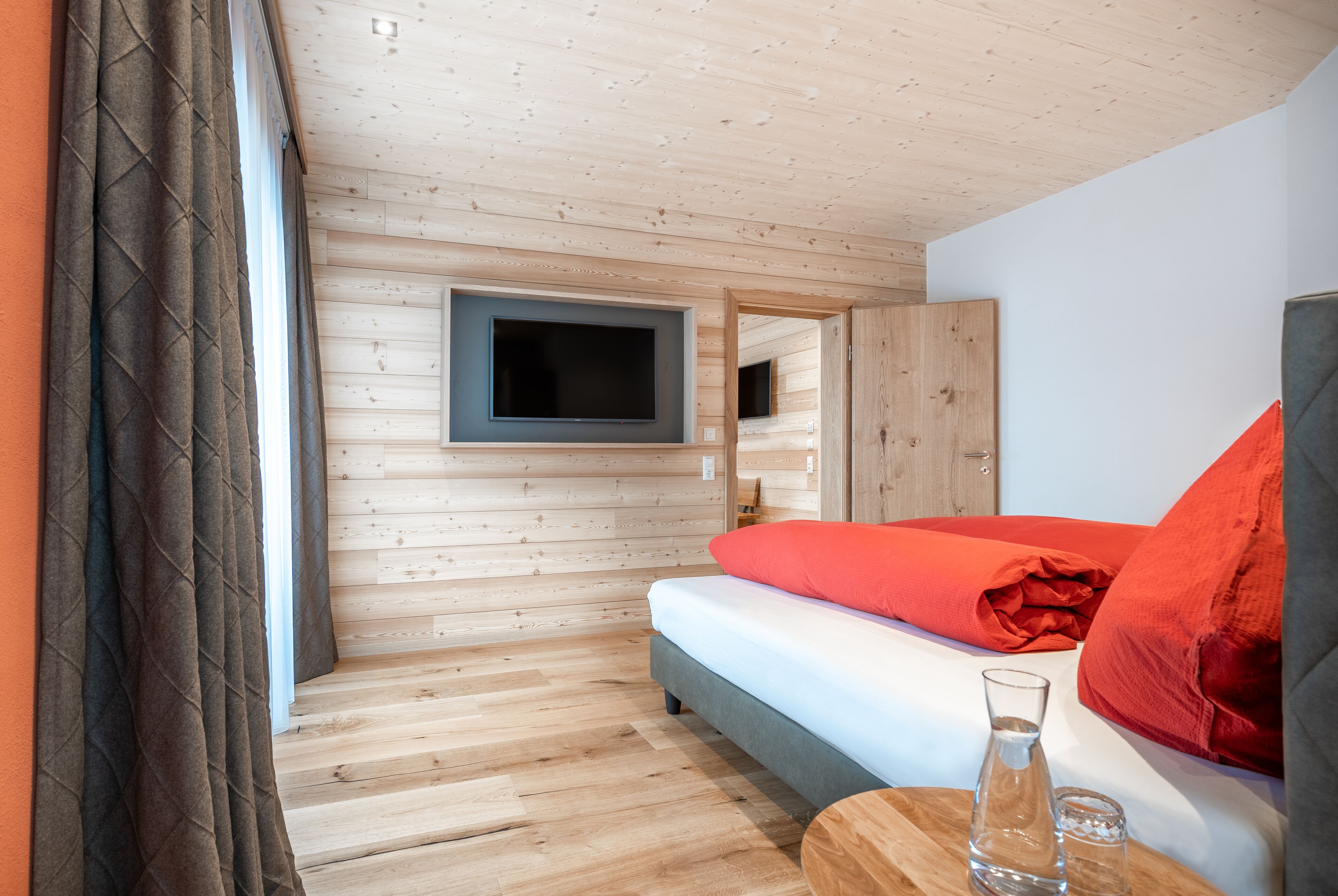 Ein Zimmer mit Holzwänden, einem Bett, einem Flachbildfernseher und einem kleinen Tisch mit Glas und Kerze.