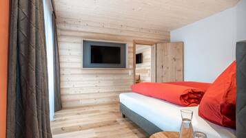 Ein Zimmer mit Holzwänden, einem Bett, einem Flachbildfernseher und einem kleinen Tisch mit Glas und Kerze.