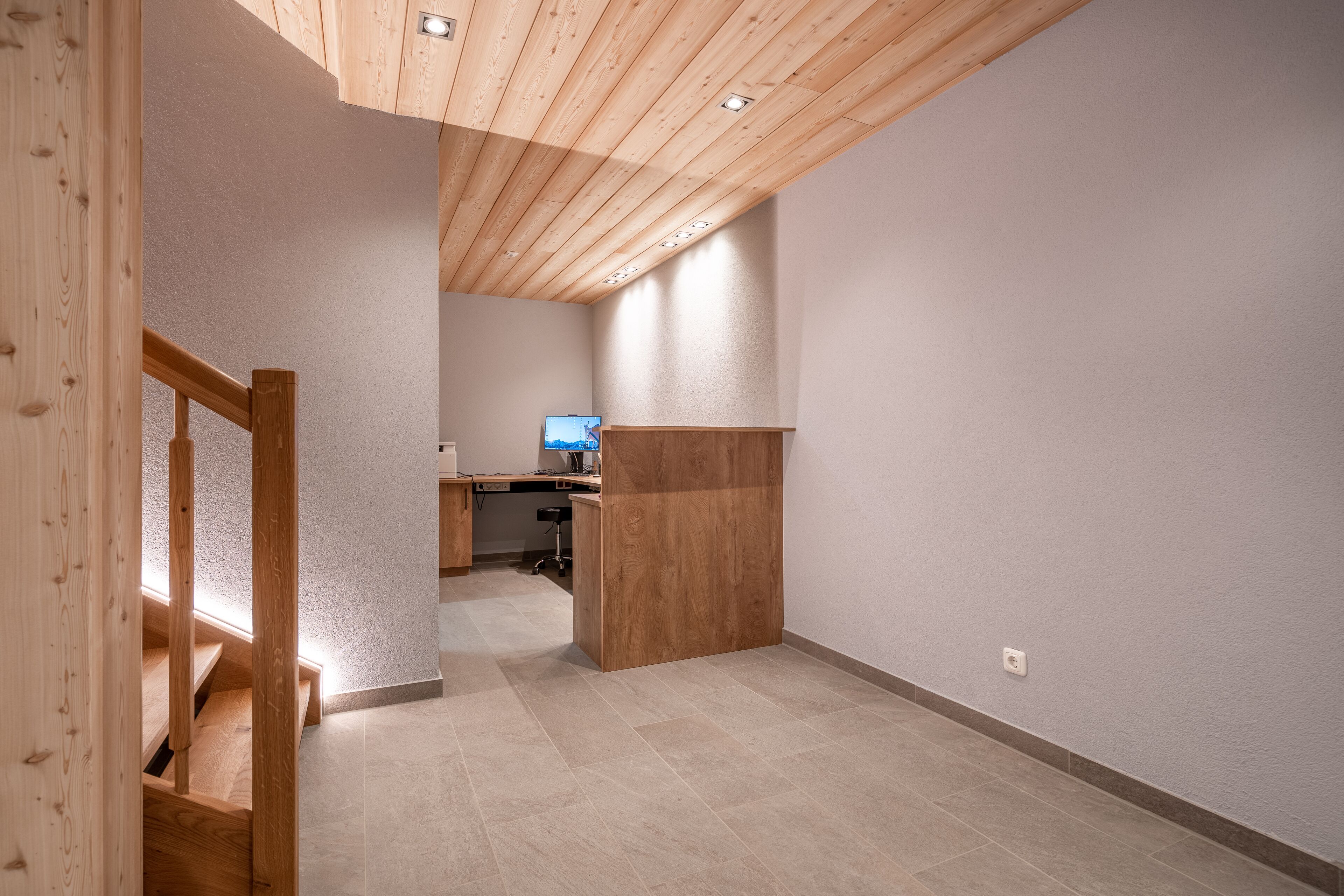 A spacious room with a wooden staircase, a desk, and a television in the background.