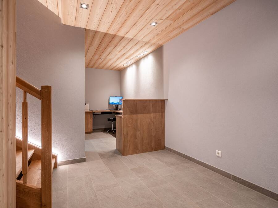 Une pièce spacieuse avec un escalier en bois, un bureau et un téléviseur à l’arrière-plan.