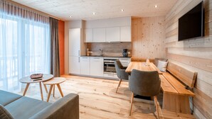 A modern kitchen with wooden cabinets and a built-in oven. There is a dining area with a wooden table and chairs, and a large window with curtains. - Naturhaus Gehren (Steeg)