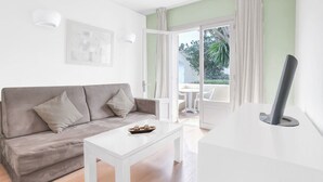 A modern living room with a grey sofa, a white coffee table, and a flat-screen TV on a white stand. - Apartment with Pool View (Manacor)