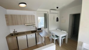 A compact kitchen with a sink, a microwave, and a small refrigerator. There is a dining table with chairs and a pendant light above it. - Apartment with Pool View (Manacor)
