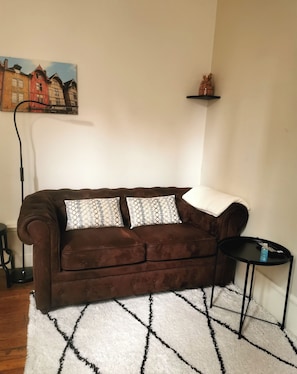 Relax in this inviting living room with a plush sofa, side table, and decorative shelf.