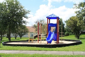 Kids can play on the playground's slide and climbing area surrounded by trees.