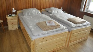 Une pièce aux murs lambrissés, avec deux lits en bois, une table de chevet et une lampe.