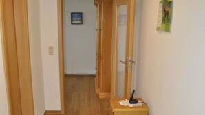 Un couloir étroit au plancher de bois, un petit banc avec un coussin, un miroir et une porte donnant sur une autre pièce.