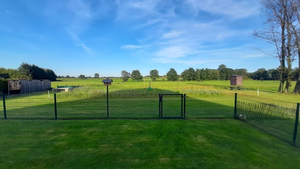 Un espace extérieur clos, avec un terrain herbeux, une petite construction et un ciel bleu dégagé.