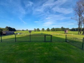 A fenced outdoor area with a grassy field, a small structure, and a clear blue sky.