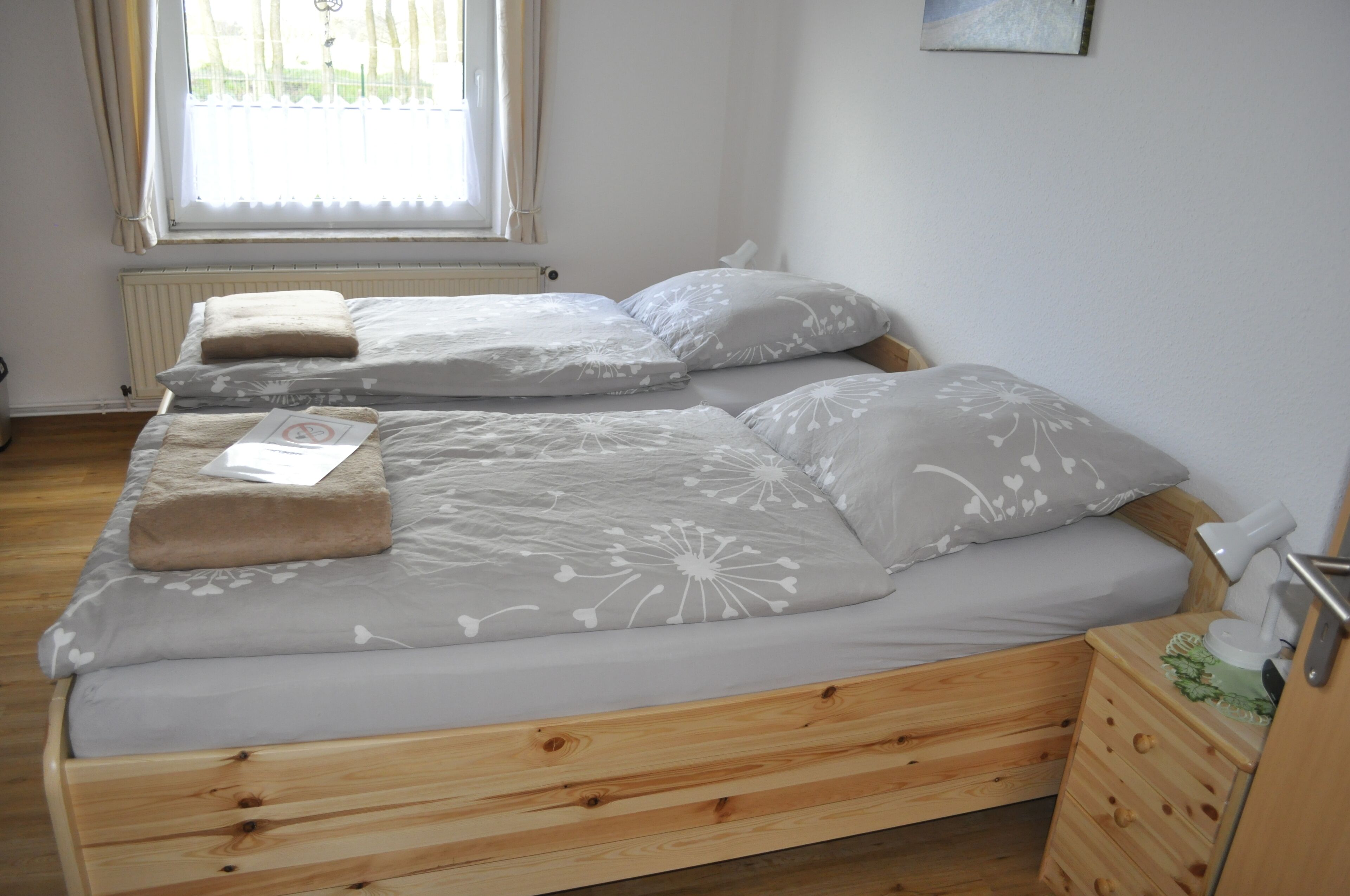 A double bed with a wooden frame, a bedside table with a drawer, and a window with curtains.