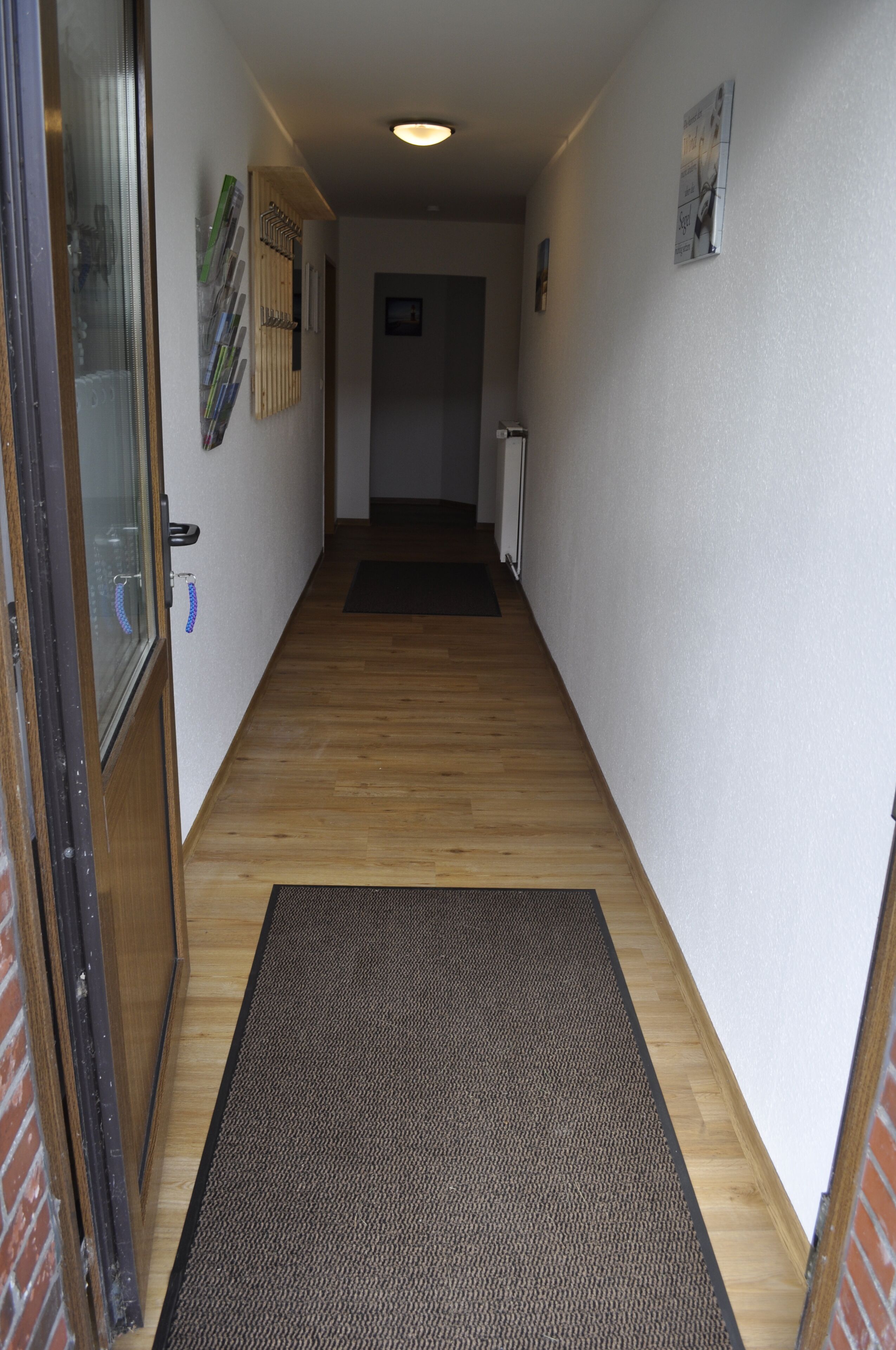 Un pasillo estrecho con piso de madera, un felpudo y una puerta con panel de vidrio.