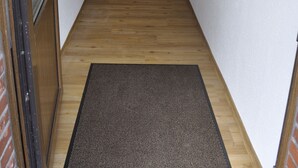 Un couloir étroit avec un plancher en bois, un paillasson et une porte dotée d’un panneau de verre.