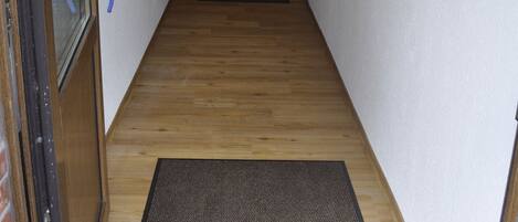 Un pasillo estrecho con piso de madera, un felpudo y una puerta con panel de vidrio.
