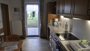 Une cuisine avec des meubles de rangement en bois, un plan de travail avec une machine à café et une vue sur l’extérieur.