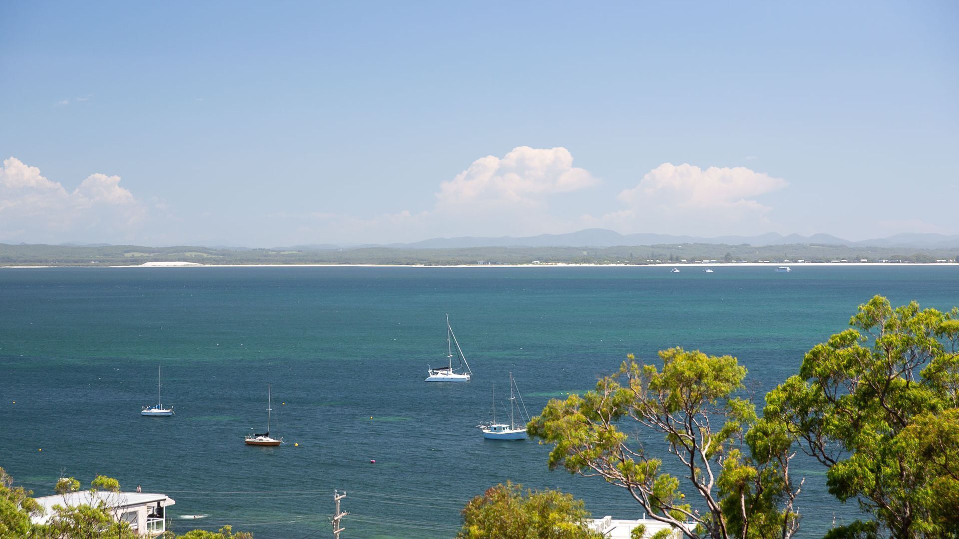 Une vue sur la côte, avec plusieurs bateaux sur l’eau, un ciel dégagé et, au loin, une terre ferme parsemée de montagnes.