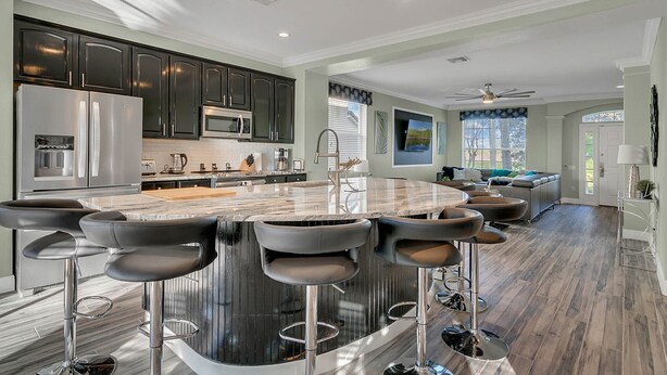 A modern kitchen with dark cabinets, a stainless steel refrigerator, and a large island with bar stools. - Disney 6BR | Theater | Themed Bedrooms | Pool/Spa (Kissimmee)