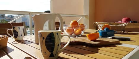 A wooden table with a white mug, a glass bowl of oranges, and a blue container with a citrus squeezer.
