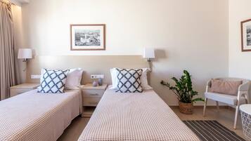 Habitación de hotel con dos camas, una mesita de noche, una lámpara, una silla y un cuadro en la pared.