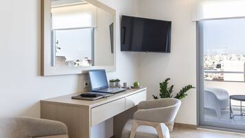 Una camera d'albergo moderna con una scrivania, due sedie, una TV a schermo piatto e un'ampia finestra con vista sulla città.