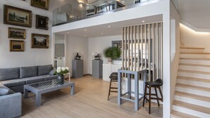 Una sala de estar moderna con un sofá gris, una mesa de centro y una barandilla de vidrio con vistas a un balcón.