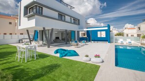 Ein modernes, zweistöckiges Haus mit Pool, Außenbereich zum Sitzen und einem gepflegten Rasen.