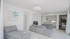 Ein modernes Wohnzimmer mit grauen Sofas, einem Flachbildfernseher und einer Küche im Hintergrund.