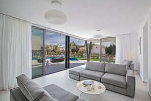 Una sala moderna con un sofá gris, una mesa de centro y vistas a una piscina y zona de estar al aire libre.