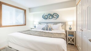 Une chambre avec un grand lit, deux tables de chevet, un élément décoratif mural et une fenêtre avec des stores.