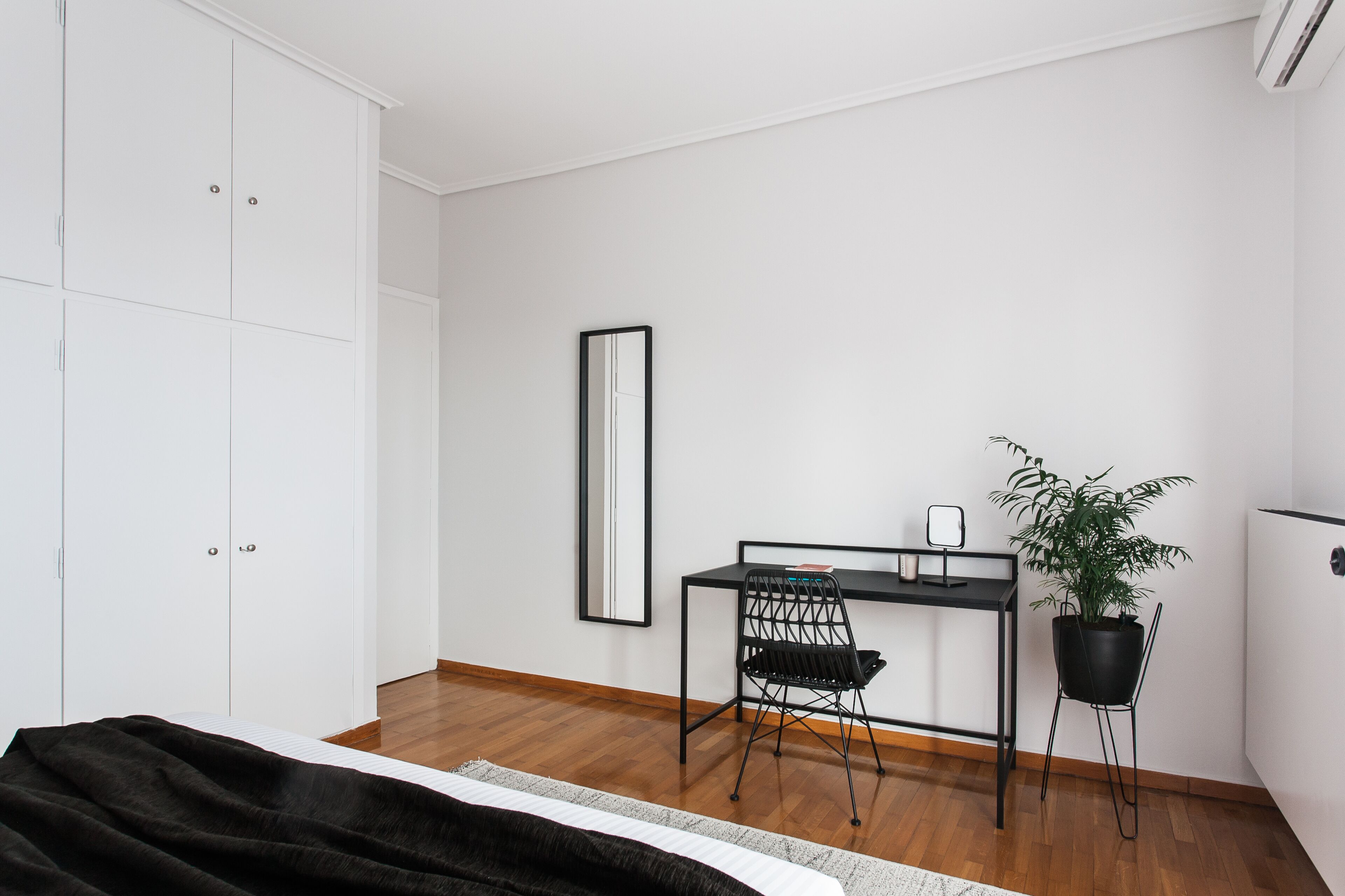 Ein Schlafzimmer mit einem Bett, einem Schreibtisch, einem Stuhl, einer Zimmerpflanze und einem Kleiderschrank.