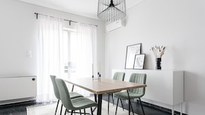 A modern dining area with a wooden table, four chairs, a white cabinet, and a black pendant light. - Spacious Apartment near HELEXPO (Marousi)