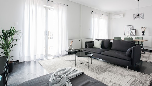 A modern living room with a black sofa, a round coffee table, and a large window with white curtains. - Spacious Apartment near HELEXPO (Marousi)