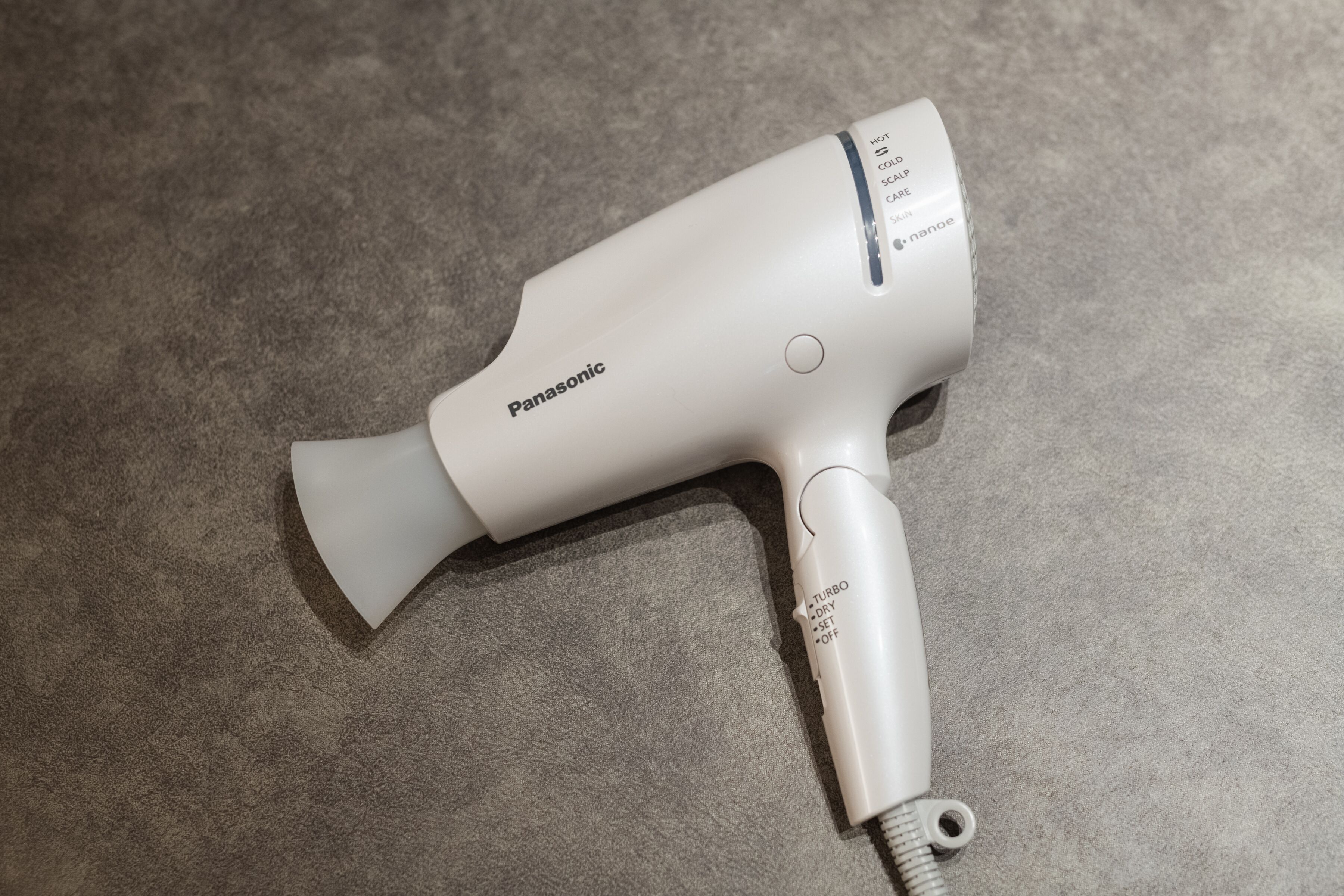 A Panasonic hair dryer with a white body and a silver nozzle, placed on a textured surface.