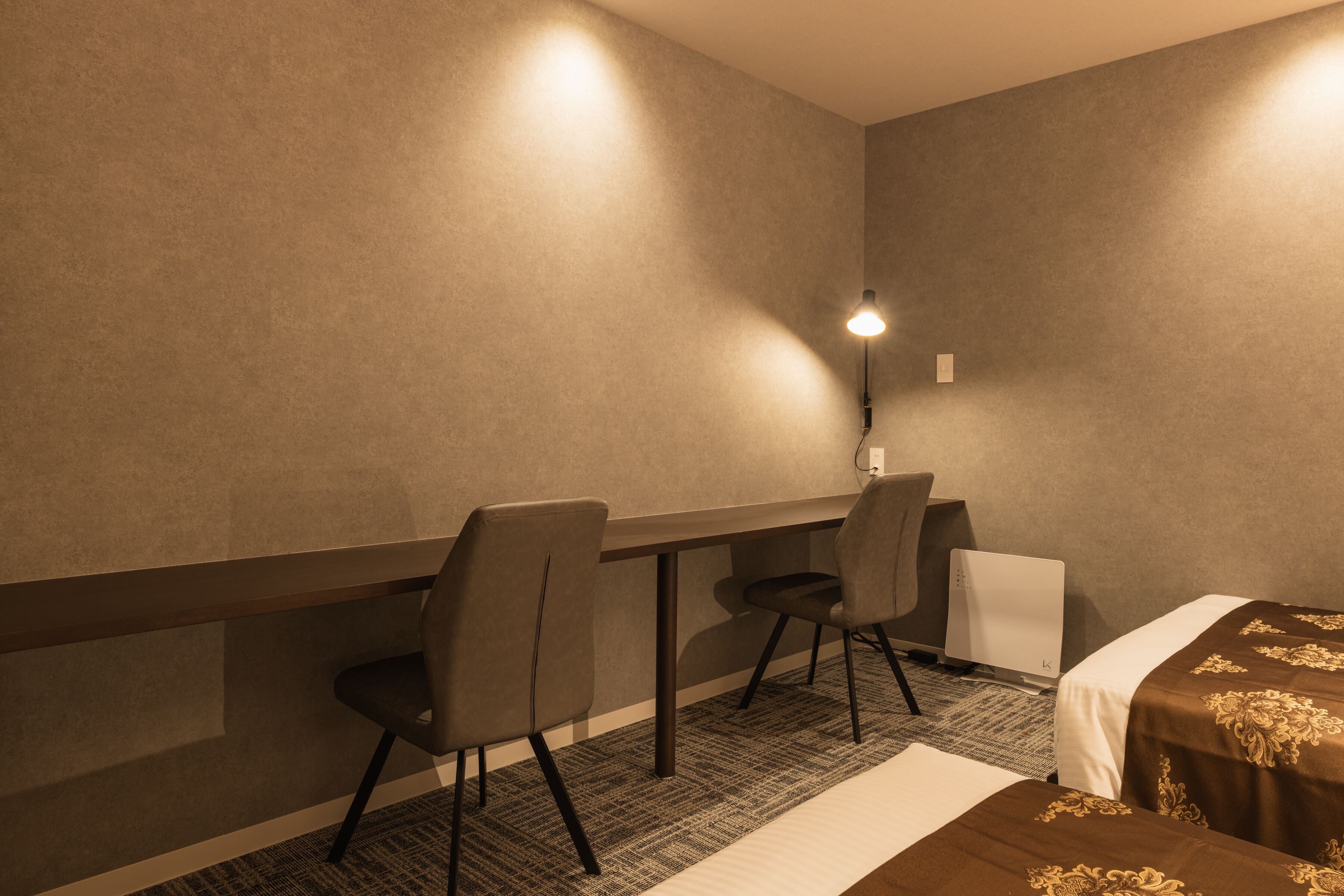 A hotel room with a bed, two chairs, a desk, and a lamp.