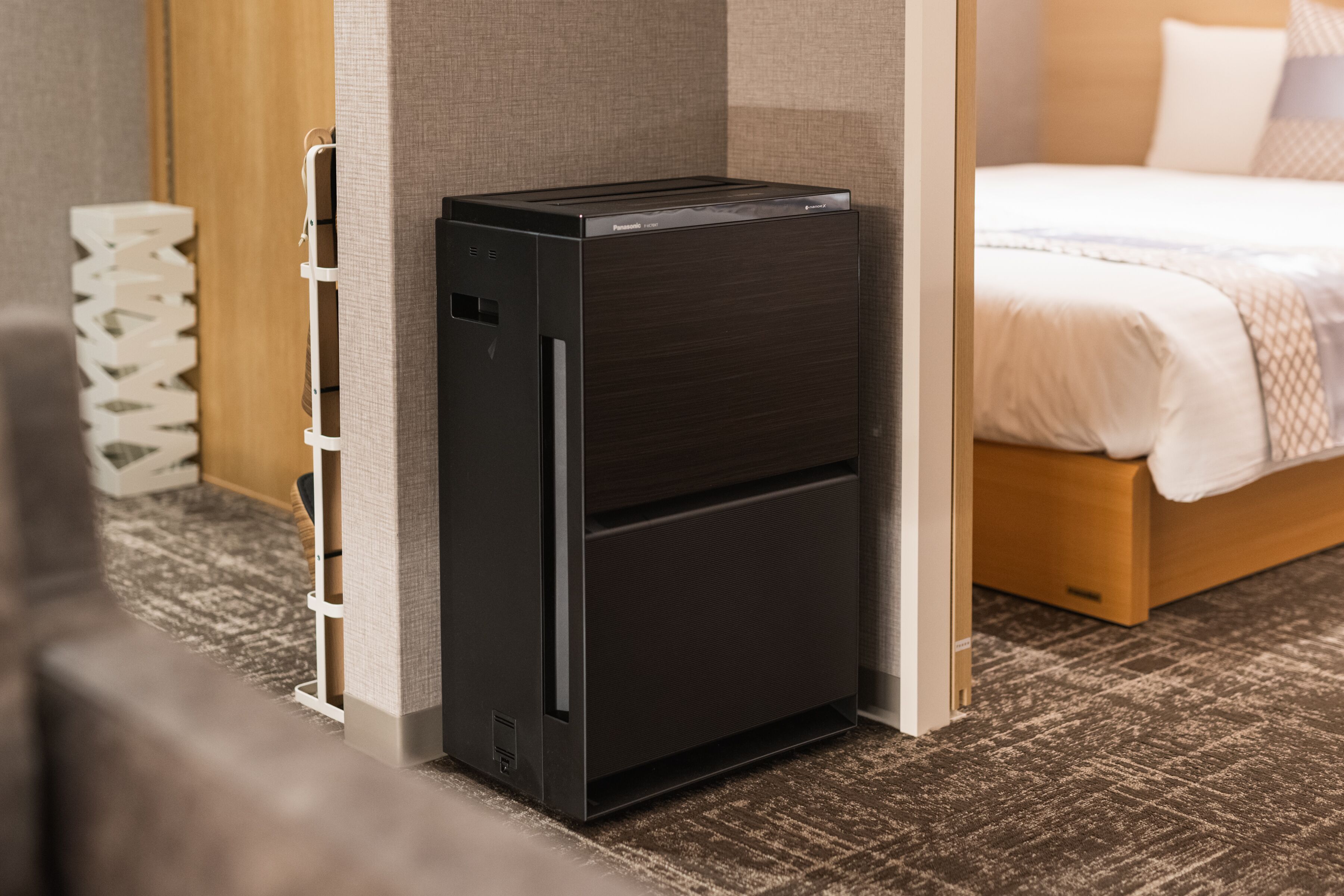 A compact, dark-colored minibar with a flat-screen TV, located in a hotel room with a wooden bed and a patterned carpet.