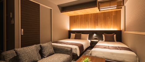 Habitación de hotel con dos camas, un sofá, una mesita y una planta en maceta.