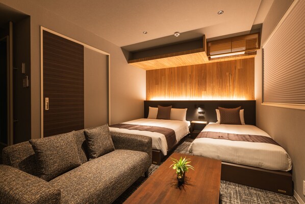 Habitación de hotel con dos camas, un sofá, una mesita y una planta en maceta.