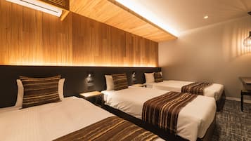 A hotel room with three beds, a wooden headboard, a desk, and a wall-mounted light fixture.