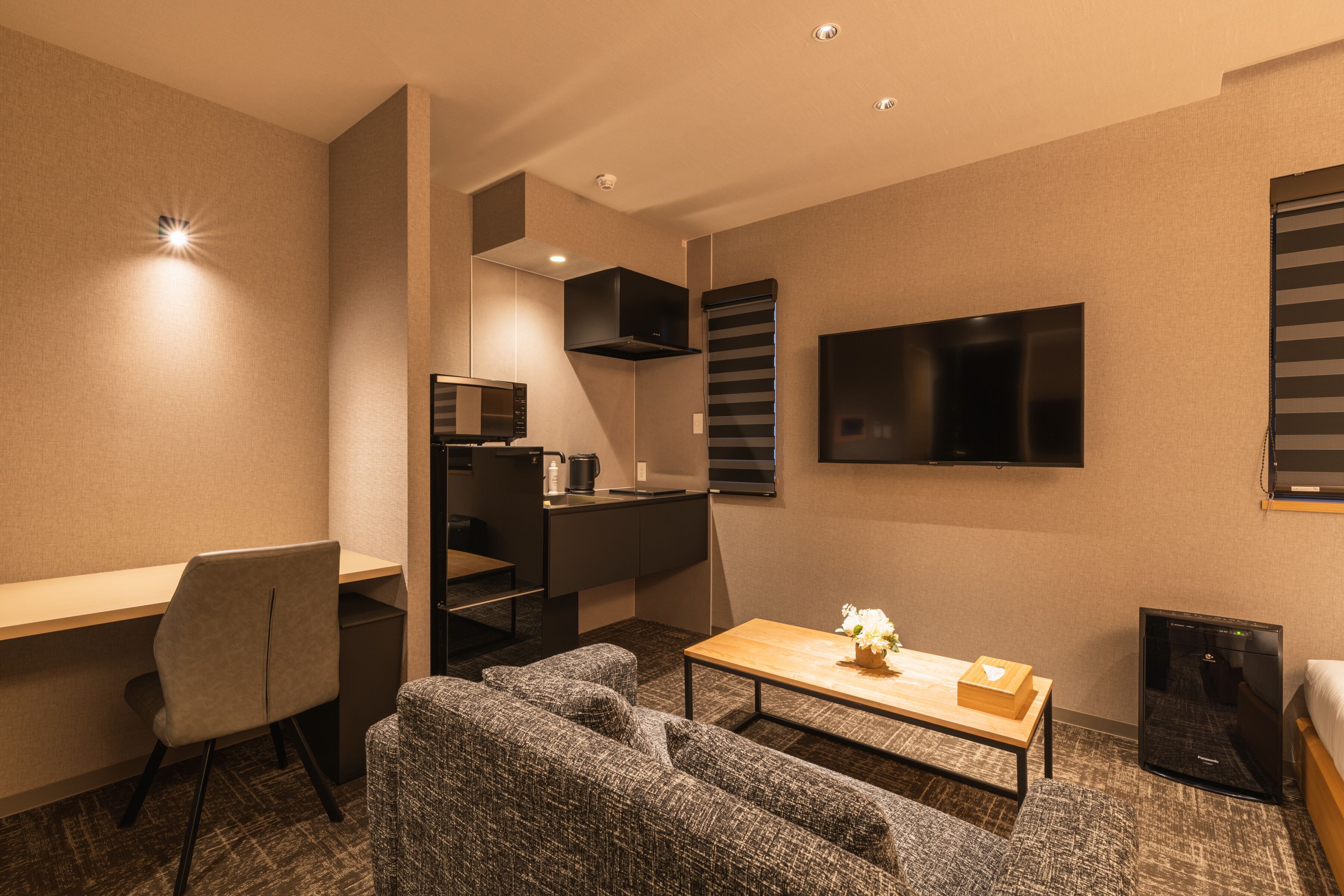 Een compacte hotelkamer met kitchenette, flatscreen televisie, een bank, bureau en een klein tafeltje met bloevas.